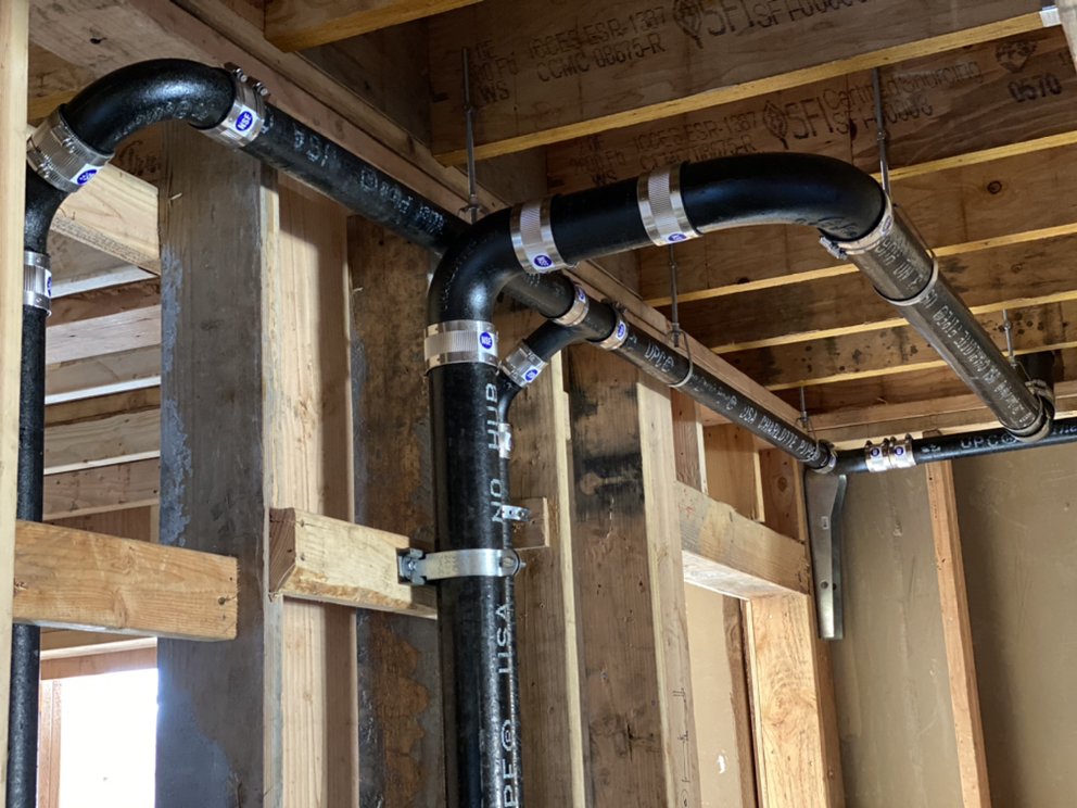 New black ABS drain, waste, and vent piping installed overhead in a home's framing